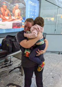 Tessa, a white autistic adult, is in an airport wearing their Sunflower lanyard. They're in distress