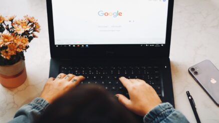 An over-the-head shot of someone using a laptop. The homepage of Google's search engine is displayed on the screen, as if the user is about to perform a search.